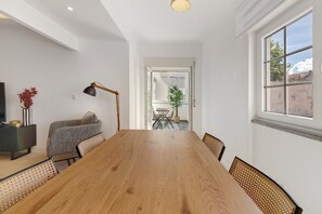 A dining area with a wooden table, chairs, a lamp, a sofa, and a TV on a stand.