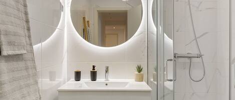 A bathroom with a glass shower enclosure, a white sink with a mirror above, and a towel rack.