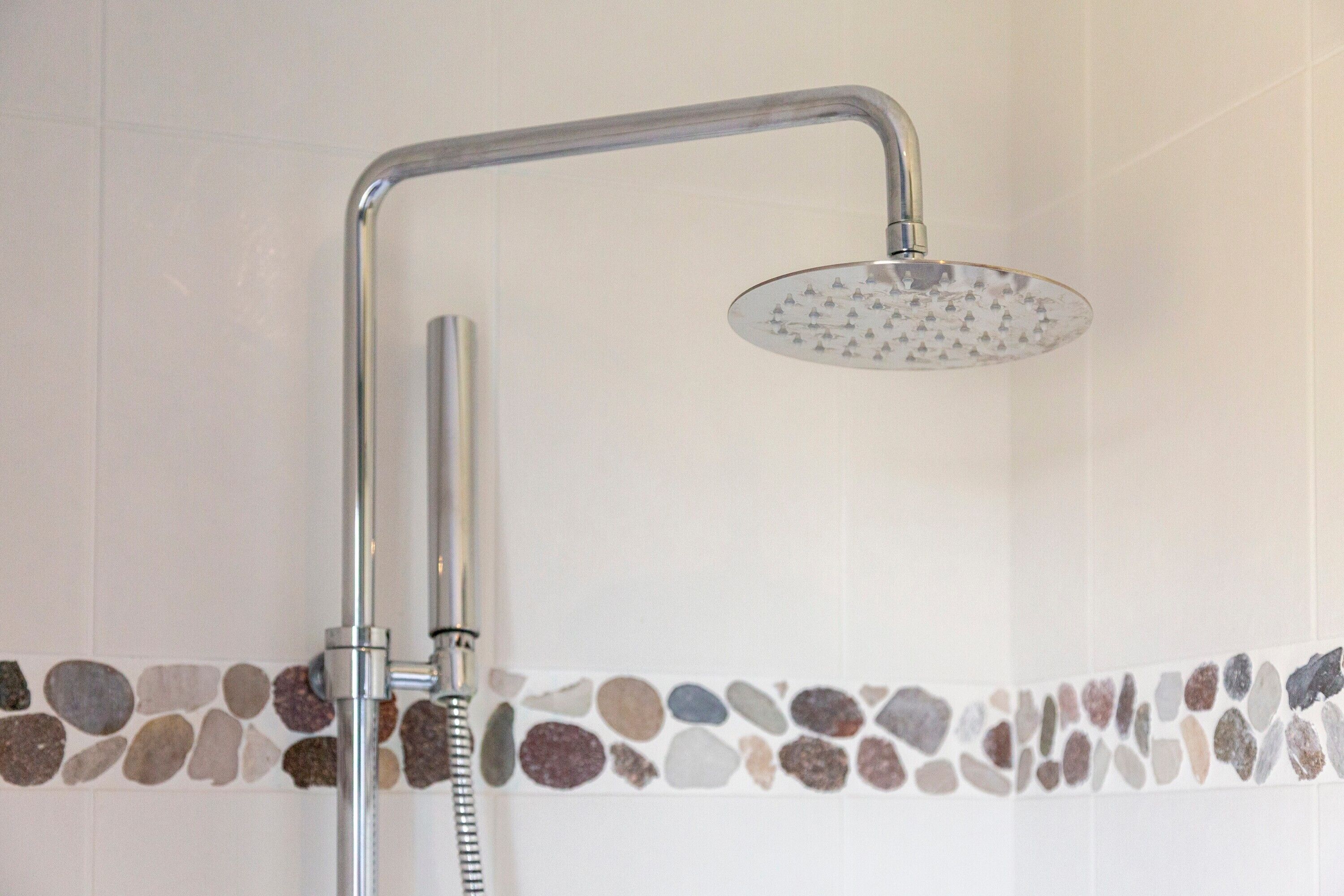 A shower with a curved head and a handheld showerhead, a wall-mounted control, and a pebble-patterned border.