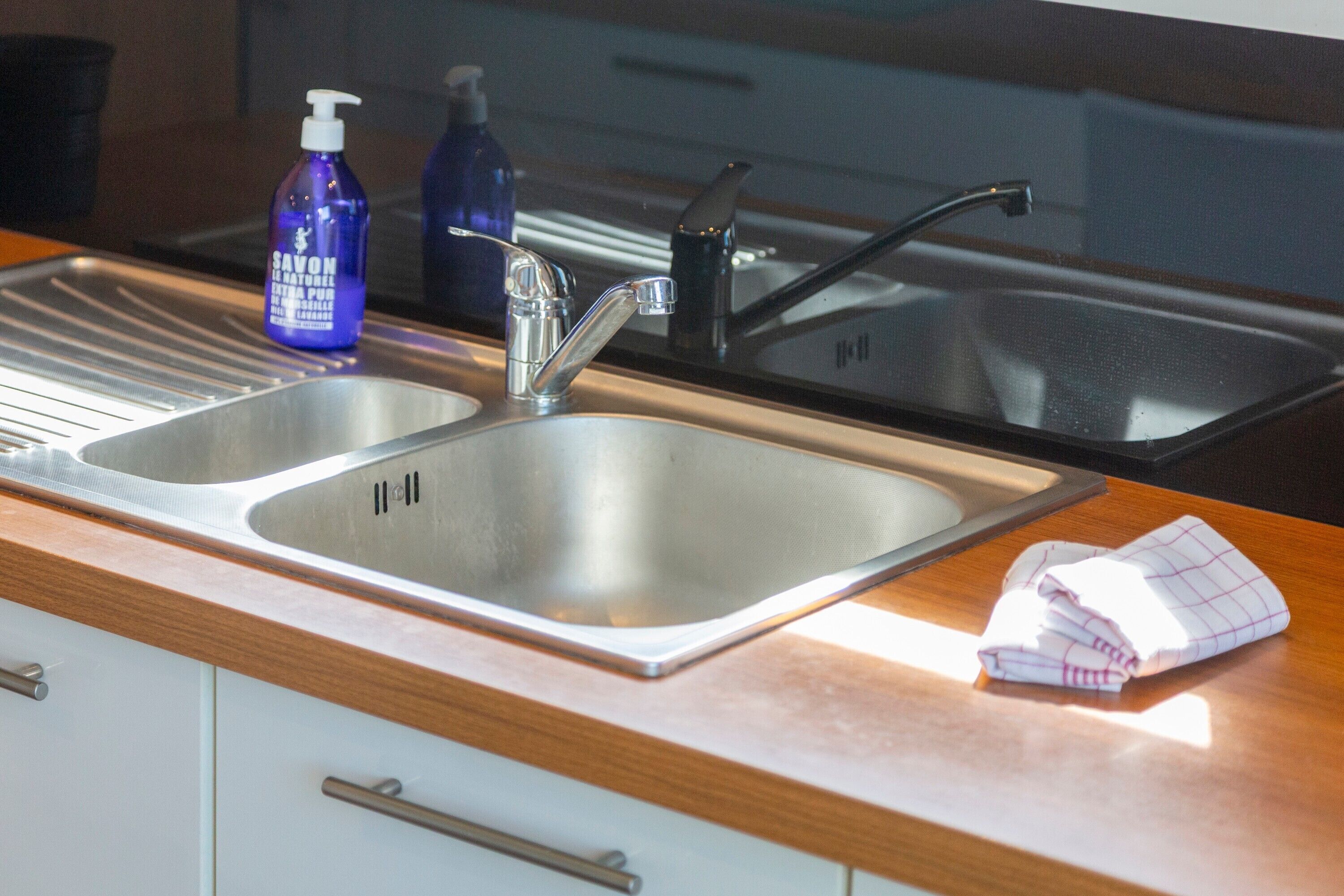 A kitchen with two stainless steel sinks, a wooden countertop, and a folded cloth.