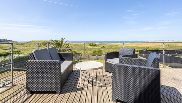 A deck with wicker furniture and a round table, overlooking a coastal landscape. - Maison Horizon – 3 Bedrooms/6 Guests – Sea View – 100m from Beach (Guilvinec)