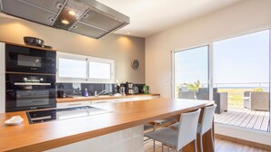 A modern kitchen with a wooden countertop, integrated appliances, and a view to the outdoor deck. - Maison Horizon – 3 Bedrooms/6 Guests – Sea View – 100m from Beach (Guilvinec)