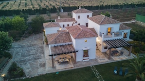 A white building with multiple sections, a patio with a table and chairs, and a surrounding garden. - Villa 'El Arroyo Ronda' with Mountain View, Wi-Fi and Air Conditioning (Ronda)