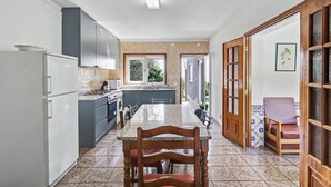 Una cocina moderna con una isla central, un comedor con mesa y sillas de madera, y vistas al exterior a través de una ventana.