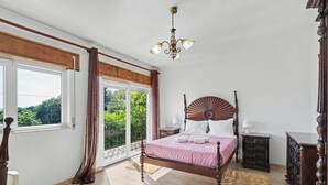 Un dormitorio con una ventana grande, una cama, una mesita de noche y un aparador.