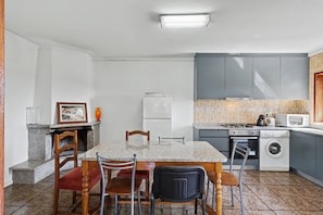 Eine kompakte Küche mit Esstisch, Stühlen, Kühlschrank, Mikrowelle, Waschmaschine und einer gefliesten Spritzschutzwand.