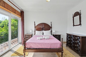 A bedroom with a bed, bedside tables, a dresser, and a large window with a view.