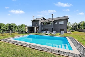 Une maison moderne à deux étages, dotée d’une piscine, d’un espace extérieur aménagé et d’une pelouse bien entretenue.