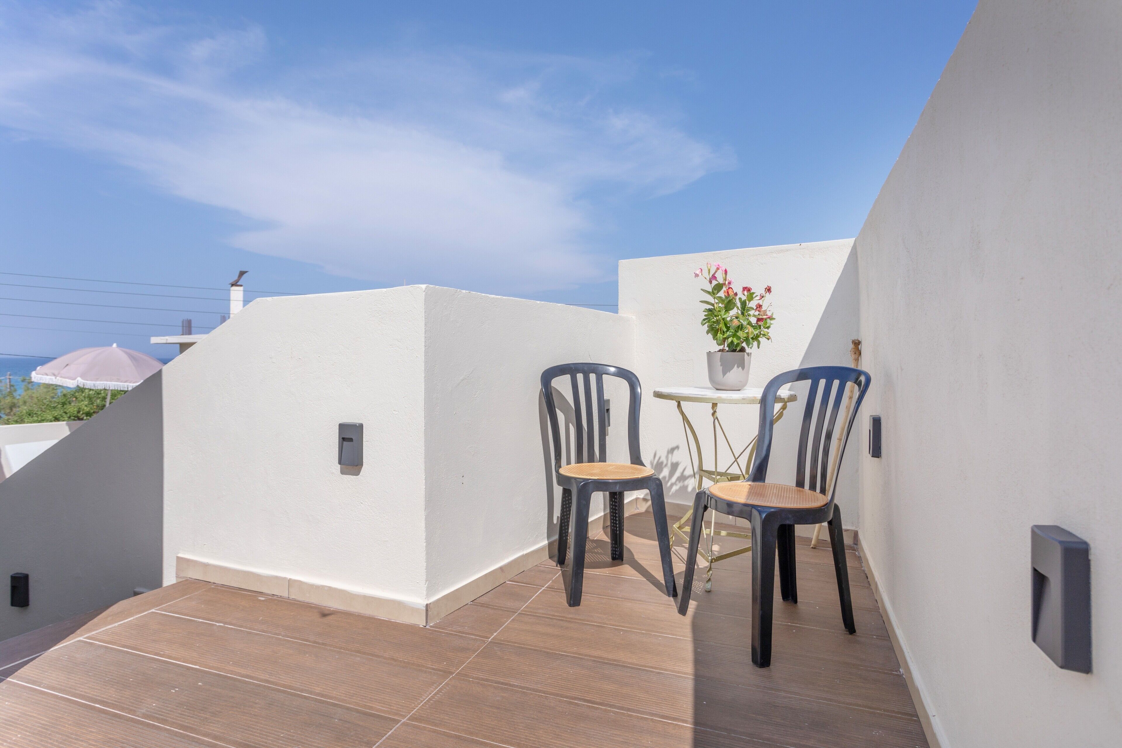 Une terrasse sur le toit avec deux chaises et une petite table, un pot de fleurs et un ciel bleu dégagé.