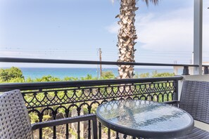 Un balcon avec une table ronde et des chaises en osier, offrant une vue sur la côte.