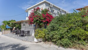 Een gebouw met een balkon, terras en een tuin vol roze bloemen.