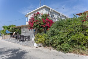 Un bâtiment doté d’un balcon, d’un espace extérieur aménagé pour s’asseoir et d’un jardin avec des fleurs roses.