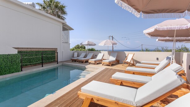 Zwembadgedeelte met ligbedden en parasols, een houten terras en uitzicht op zee.