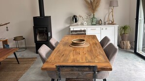 A cozy living room with a wooden dining table, a black wood-burning stove, and a white cabinet with decorative items. - Holiday Home “La P’tite Maison” with Private Terrace, Garden & Wi-Fi (Le Minihic-sur-Rance)