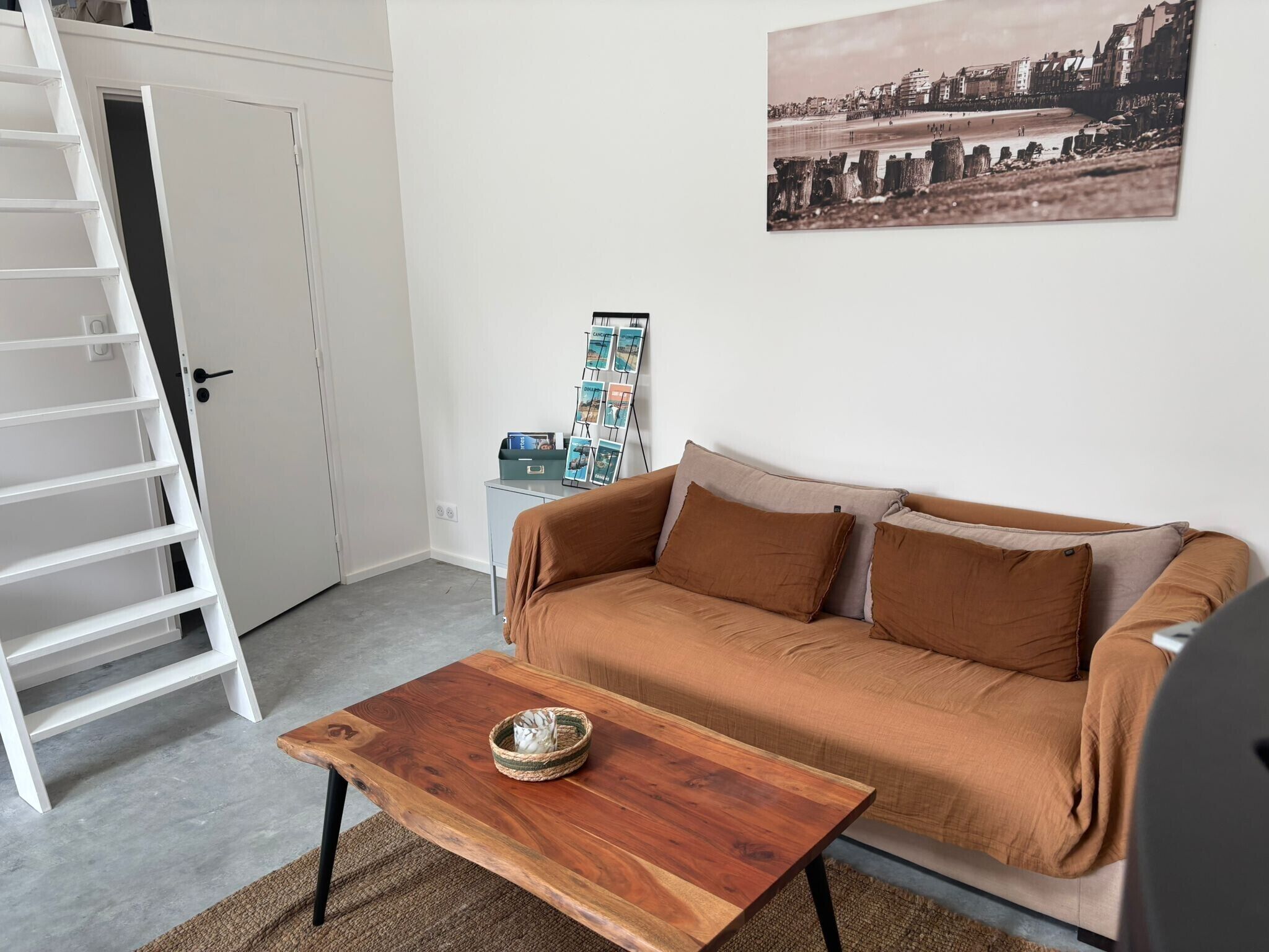A room with a wooden coffee table, a sofa, a white door, and a wall-mounted picture.