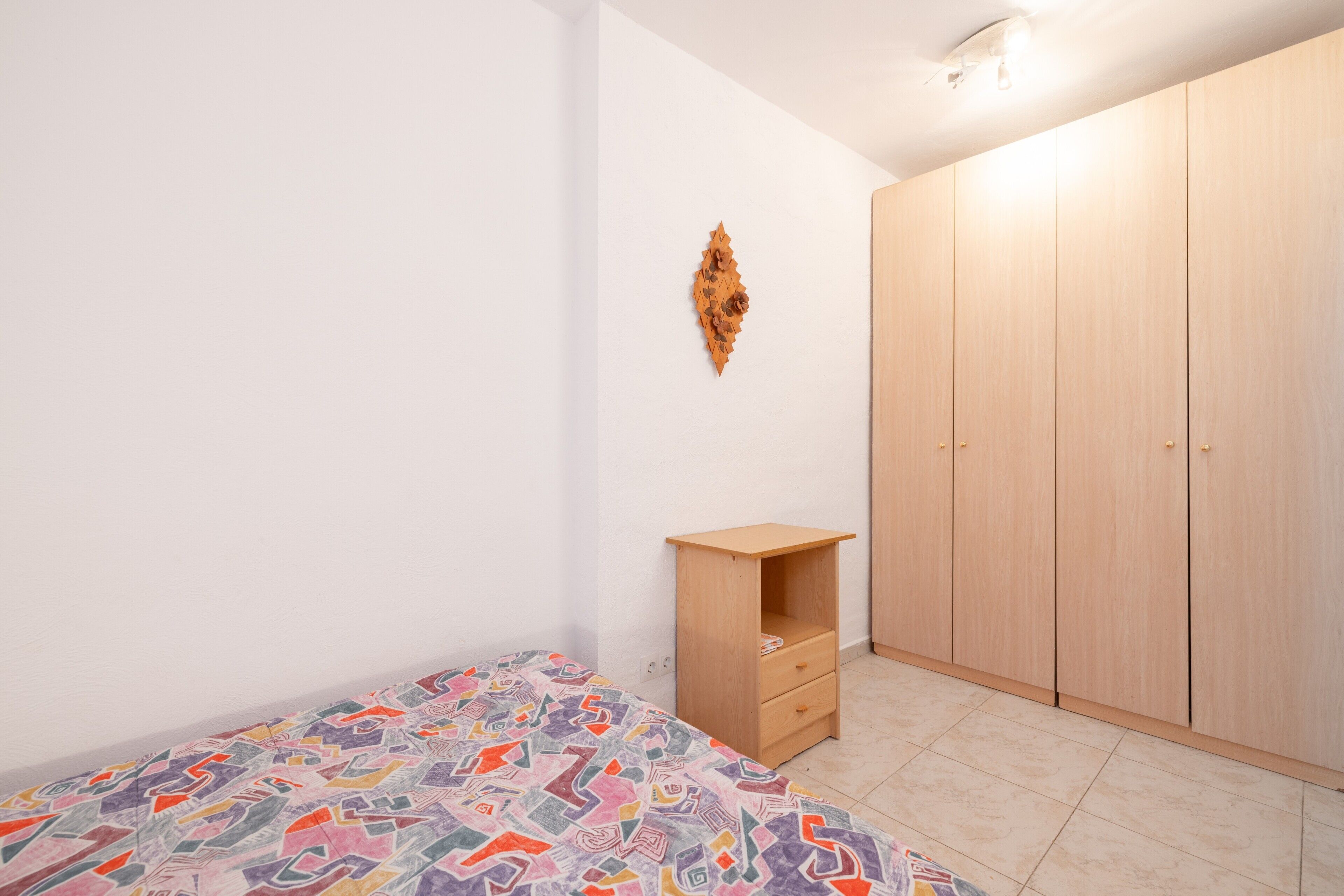 Een slaapkamer met een bed, een houten garderobe, een klein nachtkastje en een decoratie aan de muur.