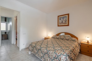 Une chambre à coucher comprenant un lit, des tables de chevet, une commode, un tableau encadré au mur et une porte donnant sur une salle de bain.