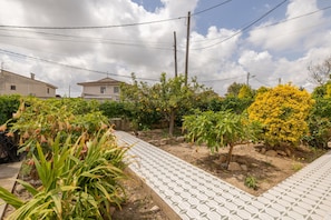 Un chemin pavé dans un espace jardin agrémenté de diverses plantes et arbres, entouré de bâtiments résidentiels.