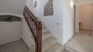 Eine Treppe mit hölzernem Geländer, einer weißen Wand mit Ziegelakzenten und einem Fliesenboden.