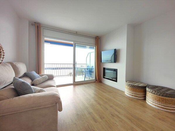 A living room with a sofa, a flat-screen TV, a fireplace, and a balcony with outdoor furniture.