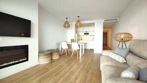 En moderne stue med pejs, en sofa med puder, et spiseområde med stole og et køkken i baggrunden.