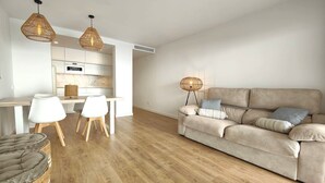 En moderne stue med sofa, to stole, et spisebord og et køkken i baggrunden.