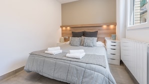 Un dormitorio moderno con una cama grande, mesitas de noche, un radiador y una ventana.