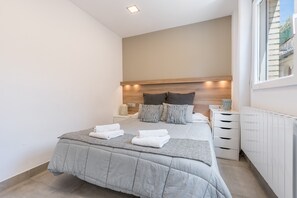Ein modernes Schlafzimmer mit einem großen Bett, Nachttischen, einer Heizung und einem Fenster.