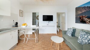 A modern kitchen with white appliances, a dining area with a white table and chairs, a green sofa with patterned cushions, and a mounted TV. - Vacation 'Beautiful Sea View and Pool Finca 1' with Shared Pool, Private Terrace and Wi-Fi (Adeje)