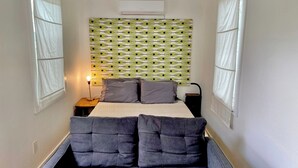 A narrow room with a bed, a headboard with a patterned design, and two chairs. - Club Casita . Unique Stay . Easy to Airport (Austin)