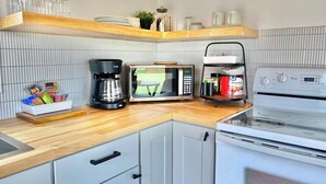 A kitchen with a microwave, coffee maker, and a stove. There are shelves with glassware and a plant. - Club Casita . Unique Stay . Easy to Airport (Austin)