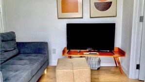 A living room with a grey sofa, a wooden coffee table, a flat-screen TV, and abstract wall art. - Club Casita . Unique Stay . Easy to Airport (Austin)