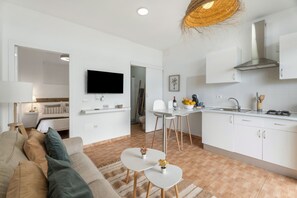 A modern, minimalist living room with a sofa, a dining area with a table and chairs, a kitchen with white cabinets and a stove, and a flat-screen TV mounted on the wall. - Vacation 'Beautiful Sea View and Pool Finca 2' with Shared Pool, Private Terrace and Wi-Fi (Adeje)