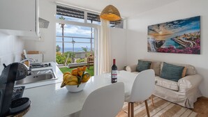 Une cuisine moderne avec un coin repas, un canapé et un tableau représentant un paysage côtier.