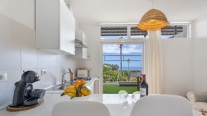 Une cuisine avec vue sur la mer, un coin repas avec des chaises, une machine à café et une bouteille de vin posée sur le comptoir.