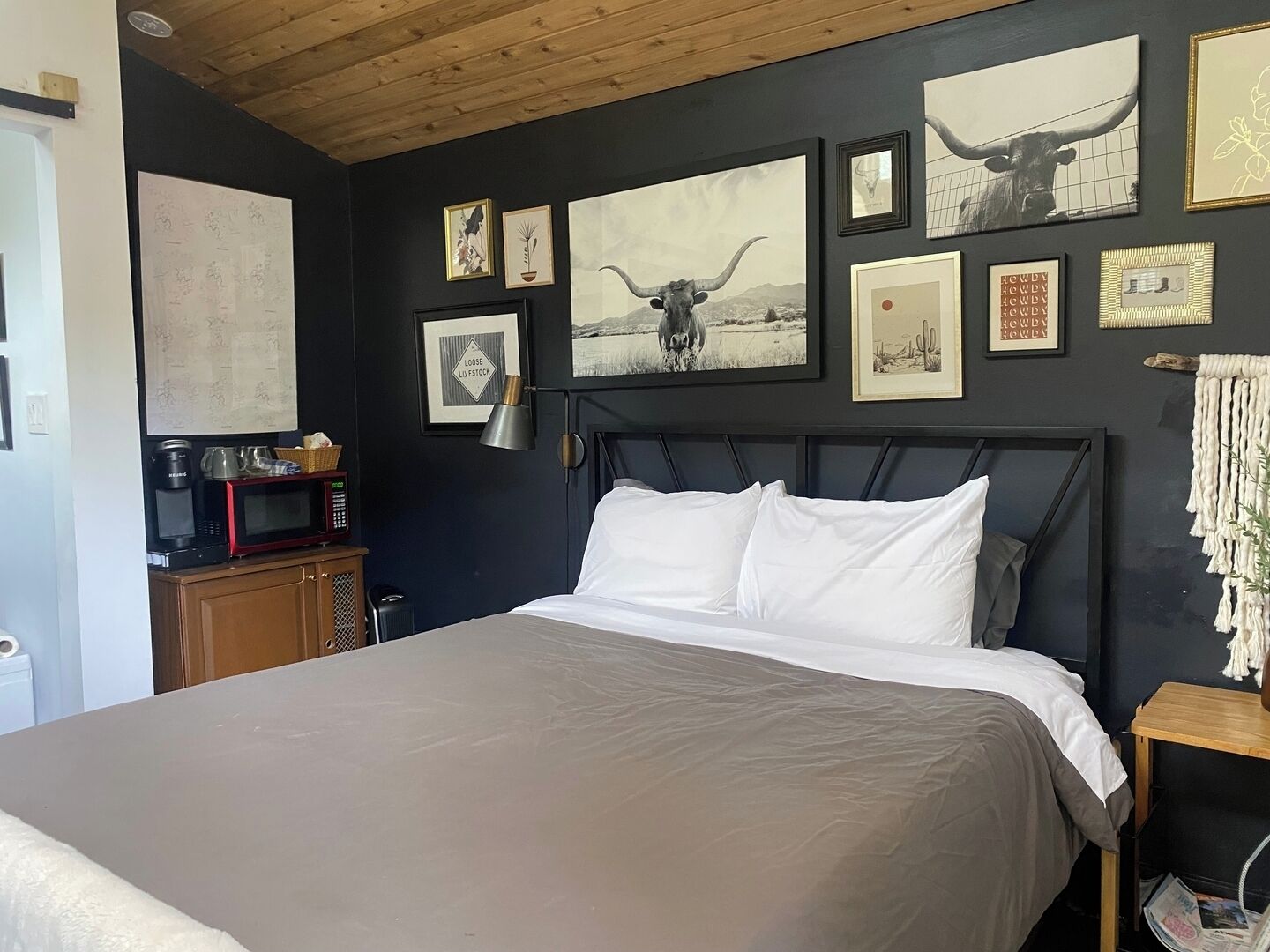 A bedroom with a large bed, a wooden headboard, and a wall decorated with various framed pictures and a map.