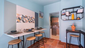 Uma cozinha moderna com área de bar, apresentando uma obra de arte geométrica, um banquinho de madeira e uma prateleira de metal preta com livros e uma planta.