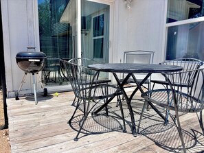 Une terrasse extérieure avec une table et des chaises rondes en métal, un barbecue et une plateforme en bois.