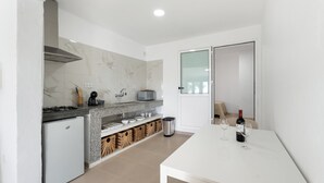 Een moderne keuken met een wit aanrecht, een inbouwfornuis, een kleine koelkast en een eettafel met twee wijnglazen en een fles.