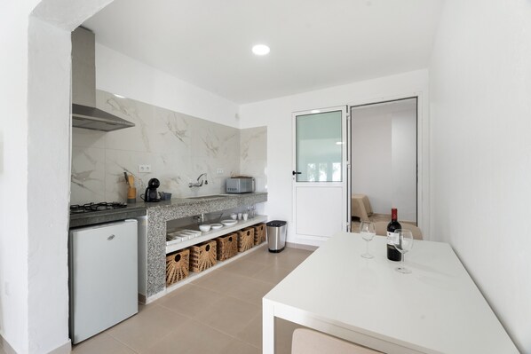 A modern kitchen with a white countertop, a built-in stove, a small refrigerator, and a dining table with two wine glasses and a bottle. - Vacation 'Beautiful Sea View and Pool Finca 4' with Shared Pool, Private Terrace and Wi-Fi (Adeje)