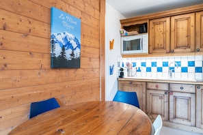 Une table de salle à manger en bois avec des chaises, un coin cuisine avec des meubles en bois, un four à micro-ondes et un pare-feu en carreaux bleus et blancs.