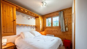 A wooden cabin bedroom with a bed, nightstand, and window with curtains.