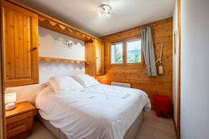 A wooden cabin bedroom with a bed, nightstand, and window with curtains. - Apartment 'La Saulire' with Mountain View, Private Terrace and Wi-Fi (Les Allues)