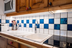 A kitchen with wooden cabinets, a white sink, and blue and white tiles. - Apartment 'La Saulire' with Mountain View, Private Terrace and Wi-Fi (Les Allues)