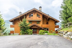 Un grand chalet en bois doté d’un balcon imposant, de fondations en pierre et offrant une vue sur la forêt environnante.
