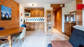 A wooden interior with a dining table, chairs, a kitchen with wooden cabinets, and a glass cabinet.