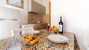 A dining table with a patterned tablecloth, plates, cutlery, a bottle of wine, and a bowl of snacks. - Cenate House Holiday Home (Nardò)