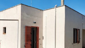 A small, single-story building with a white exterior, a red door, and a small window. - Cenate House Holiday Home (Nardò)