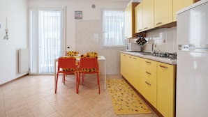 A kitchen with yellow cabinets, a white refrigerator, and a dining table with chairs. - Apartment 'San Paolo 07' with Private Terrace and Air Conditioning (Lido di Jesolo)