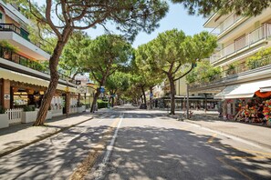 Une rue bordée d’arbres, avec des bâtiments des deux côtés, notamment des boutiques et un café.